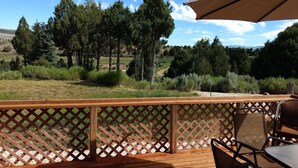 A wooden deck with a lattice railing, outdoor furniture, and a view of a forested landscape. - Panoramic Cliffs Retreat (Hatch)