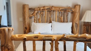Un lit en bois rustique avec une finition naturelle, un ventilateur de plafond avec éclairage intégré et une simple table de chevet avec une lampe.
