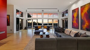 A spacious living room with a large window, a sofa, a coffee table, and artwork on the walls. - China Mountain House - Ocean Views & Modern Design (Port Orford)