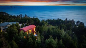 A coastal property with a red building, surrounded by dense forest, overlooking the sea. - China Mountain House - Ocean Views & Modern Design (Port Orford)