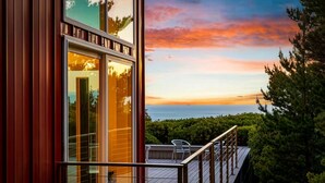 A modern building with large windows, a balcony with metal railings, and a view of the ocean at sunset. - China Mountain House - Ocean Views & Modern Design (Port Orford)