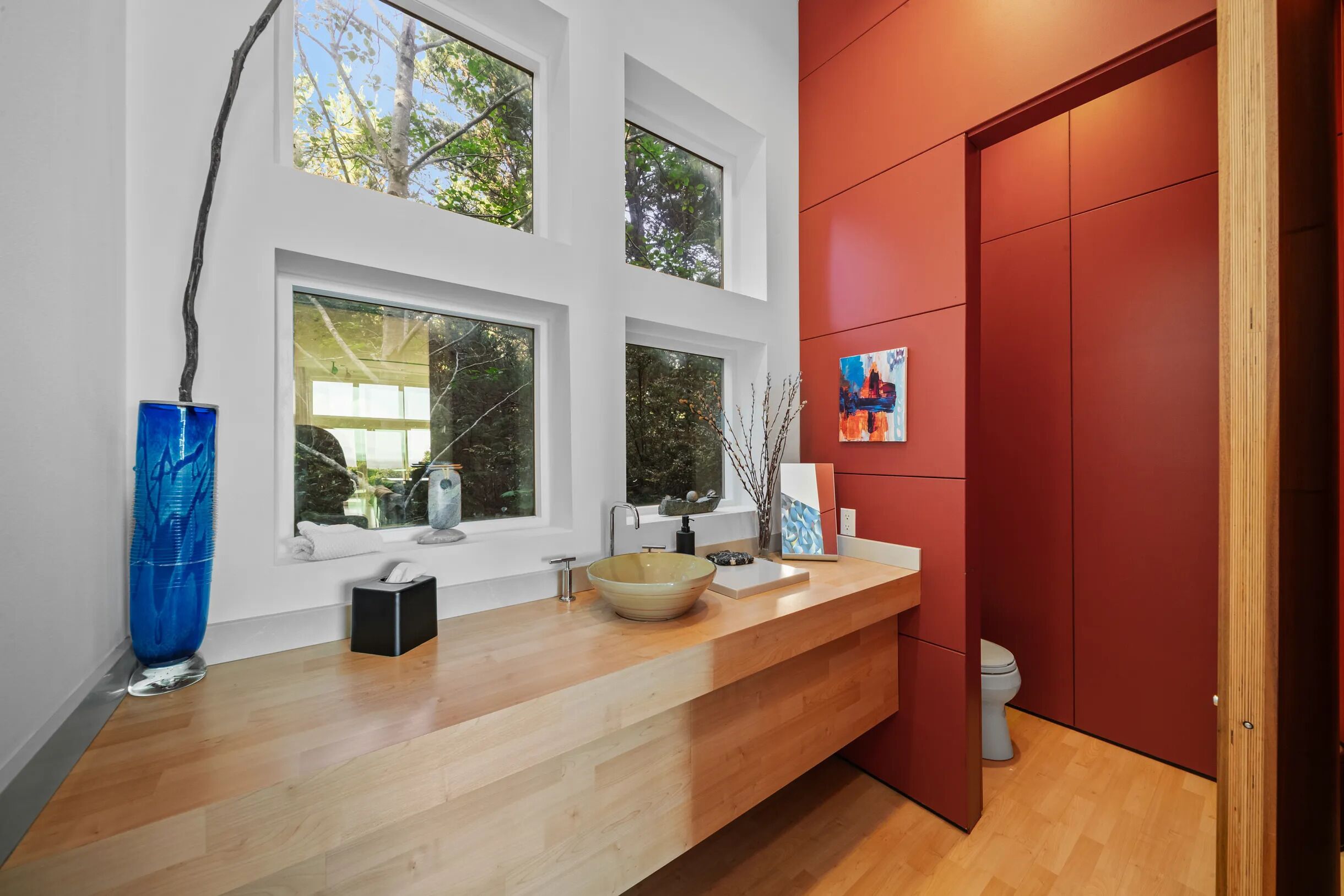 Une salle de bain moderne avec un meuble-lavabo en bois, une grande fenêtre et un mur d’accent rouge.