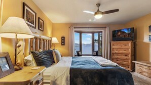 Un dormitorio con cama, lámparas de noche, cómoda, televisor y vistas al exterior.