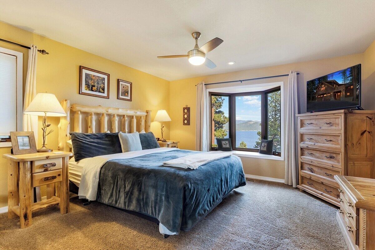 Een slaapkamer met een bed, nachtkastjes, een plafondventilator, een raam met uitzicht en een televisie op een houten kast.
