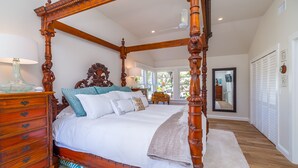 Uma cama com dossel e estrutura de madeira, um aparador com gavetas e um espelho na parede.