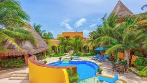 Ein Resort-Poolbereich mit einem zentralen Pool, Liegestühlen und Palmen.