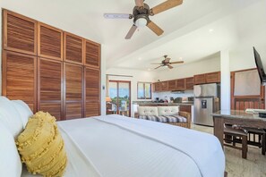 A hotel room with a bed, a wooden partition, a kitchenette, and a ceiling fan.