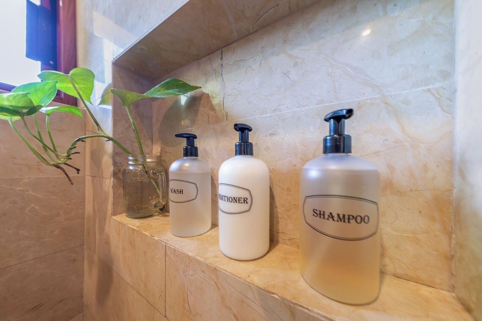 A bathroom shelf with three bottles labeled 'WASH,' 'CONDITIONER,' and 'SHAMPOO.'