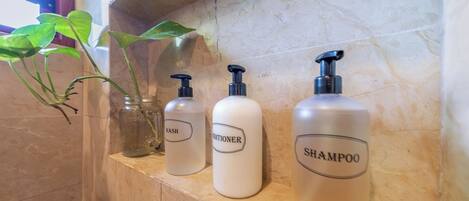 A bathroom shelf with three bottles labeled 'WASH,' 'CONDITIONER,' and 'SHAMPOO.'