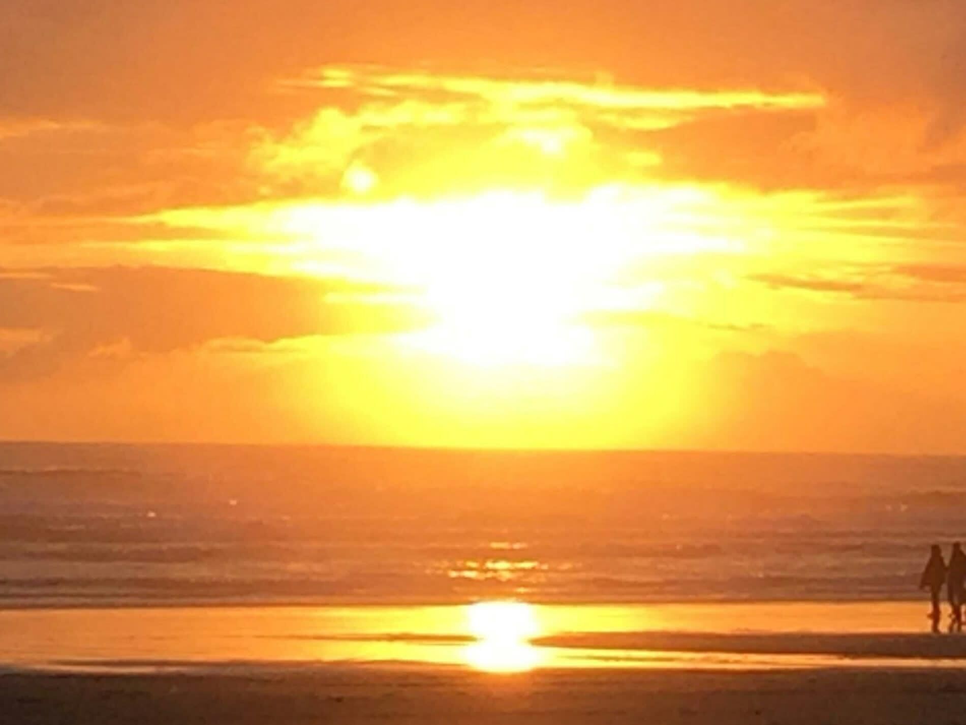 Un atardecer sobre el océano con siluetas de personas caminando por la playa.