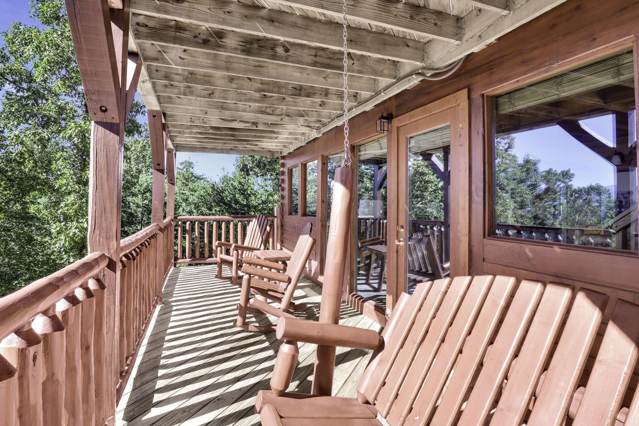 A wooden deck with chairs and a table, surrounded by trees.