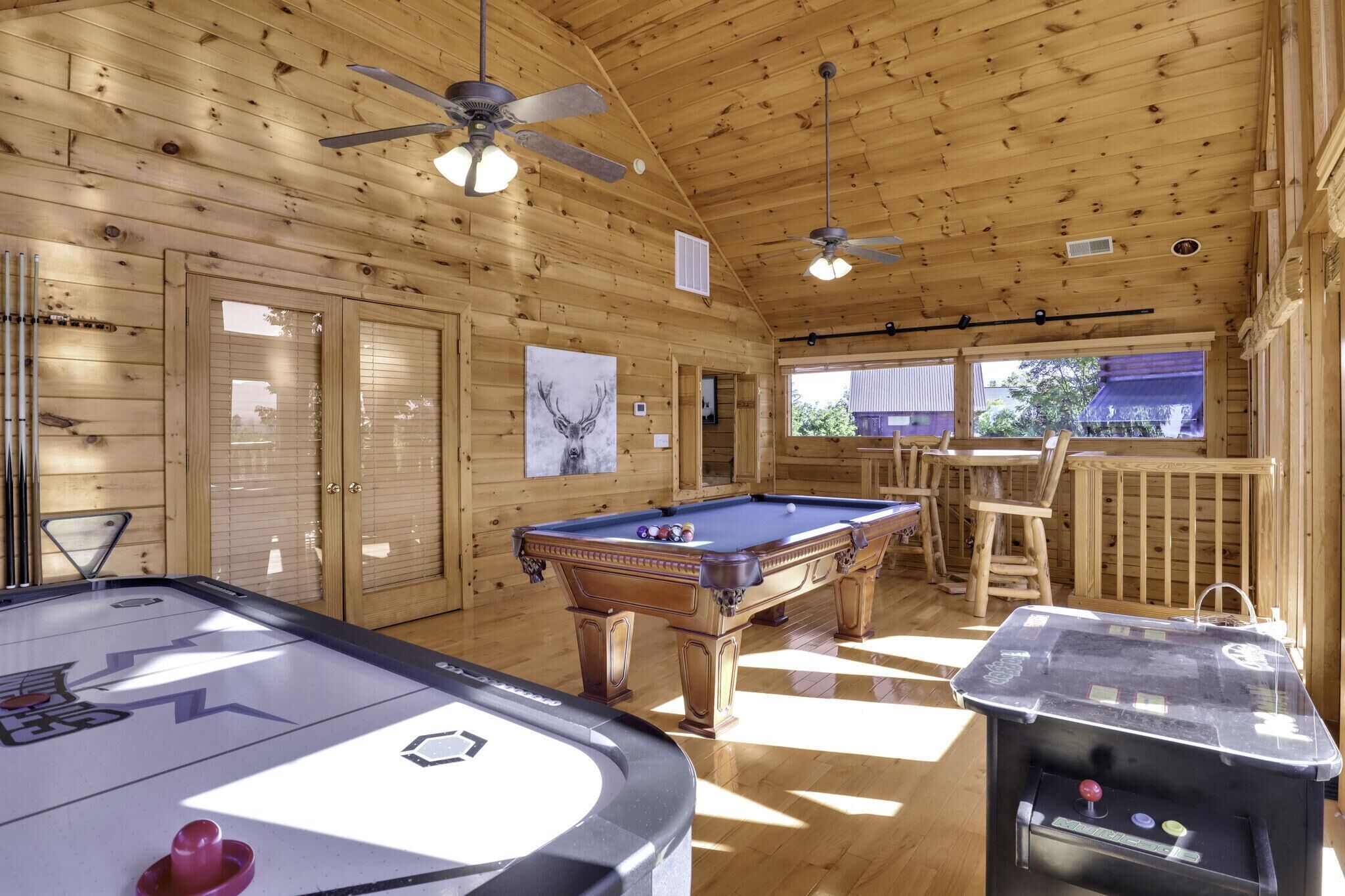 A wooden cabin with a pool table, a shuffleboard table, and a bar area.