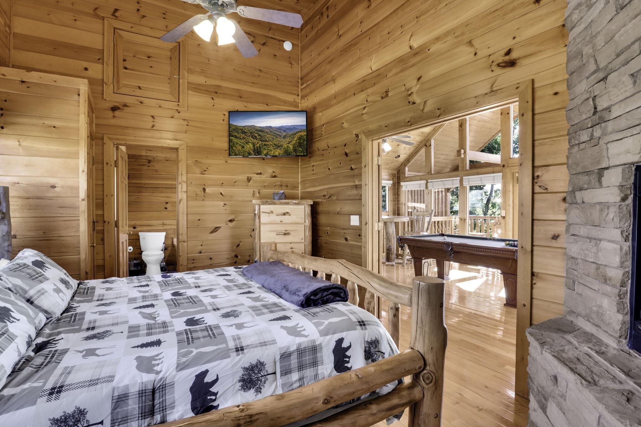 Ein Schlafzimmer einer Holzhütte mit Bett, Deckenventilator, Fernseher und Blick ins Freie.