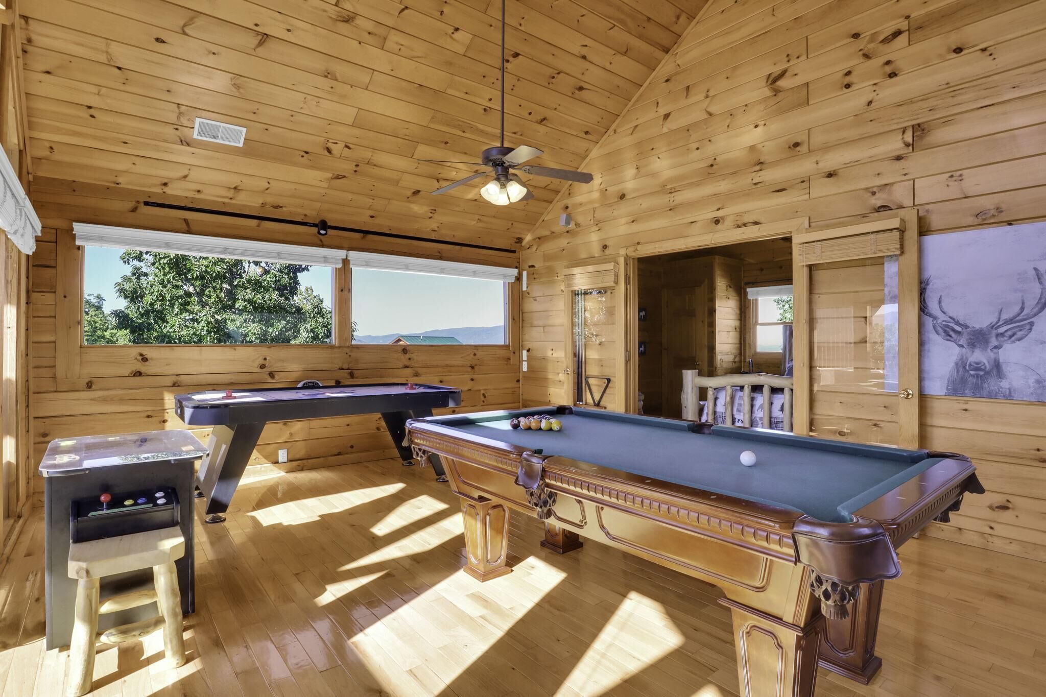 A wooden cabin with a pool table, another pool table, a billiards table, and a ceiling fan.