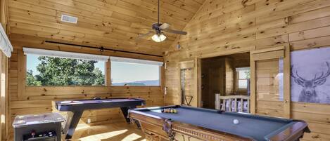 A wooden cabin with a pool table, another pool table, a billiards table, and a ceiling fan.