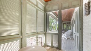 Eine überdachte Veranda mit weißen Fensterläden, einer hölzernen Bank und Blick ins Freie.