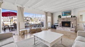 Un vaste salon doté d’une cheminée, un coin repas avec des sièges extérieurs et de grandes fenêtres offrant une vue sur le quartier.