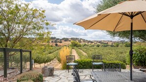 Une terrasse avec un sol en pierre, deux chaises, une table et un parasol.