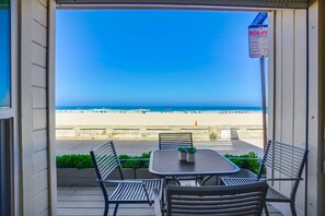A balcony with a view of a beach, a table with chairs, and a sign indicating regulations.