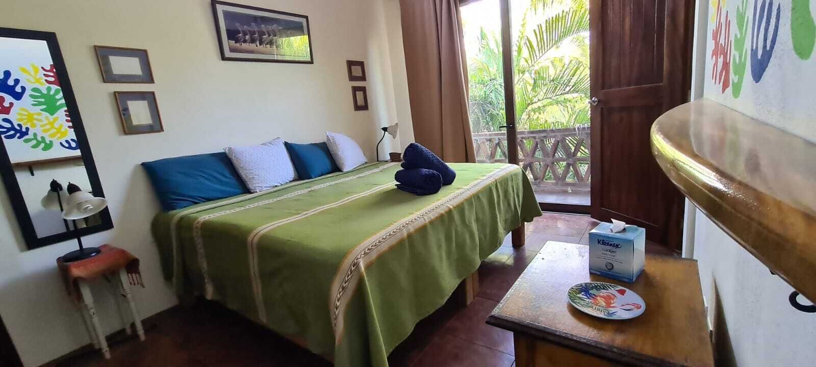 A room with a bed, a table with a box, and a view of greenery outside.