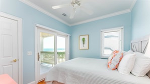 A bedroom with a bed, a door, a window with blinds, a ceiling fan, and a view of the outdoors.