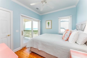 A bedroom with a bed, a door, a window with blinds, a ceiling fan, and a view of the outdoors.