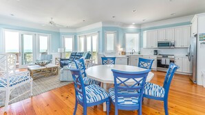 A spacious kitchen with white cabinets, a dining area with blue chairs, and a view of the ocean through large windows.
