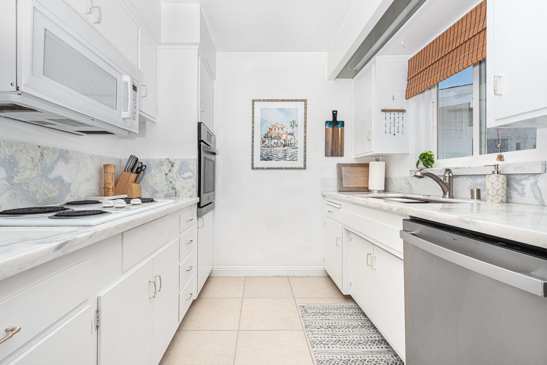 A modern kitchen with white cabinetry, a marble countertop, and stainless steel appliances.