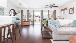 Amplia sala de estar con sofá, muebles de madera, ventilador de techo y vistas por grandes puertas de vidrio.