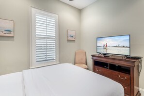 Une chambre à coucher avec un lit, une télévision, une chaise et une fenêtre avec des stores.