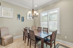 A dining room with a wooden table and chairs, a chandelier, and a window with blinds.
