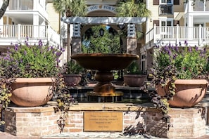 Une cour intérieure avec une fontaine centrale, entourée de plantes en pot et d’une plaque portant une citation.