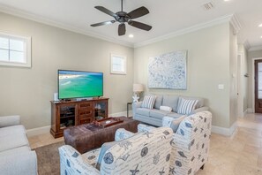 Ein Wohnzimmer mit Flachbildfernseher, Deckenventilator, Sofa, Couchtisch und einem Bild an der Wand.