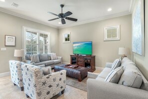 Un salon comprenant un canapé, deux fauteuils, une table basse, un téléviseur et un ventilateur de plafond.