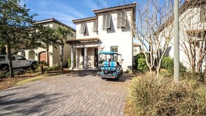 Una casa de dos pisos con entrada pavimentada, un vehículo estacionado y mobiliario exterior.