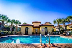 A pool area with a clear blue pool, a building with a tiled roof, and palm trees.