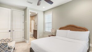 Une chambre à coucher avec un grand lit, une chaise, un ventilateur de plafond et une porte donnant sur une salle de bain.