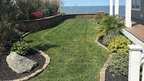 Een verzorgd gazon met een stenen muur, diverse planten en uitzicht op de oceaan.