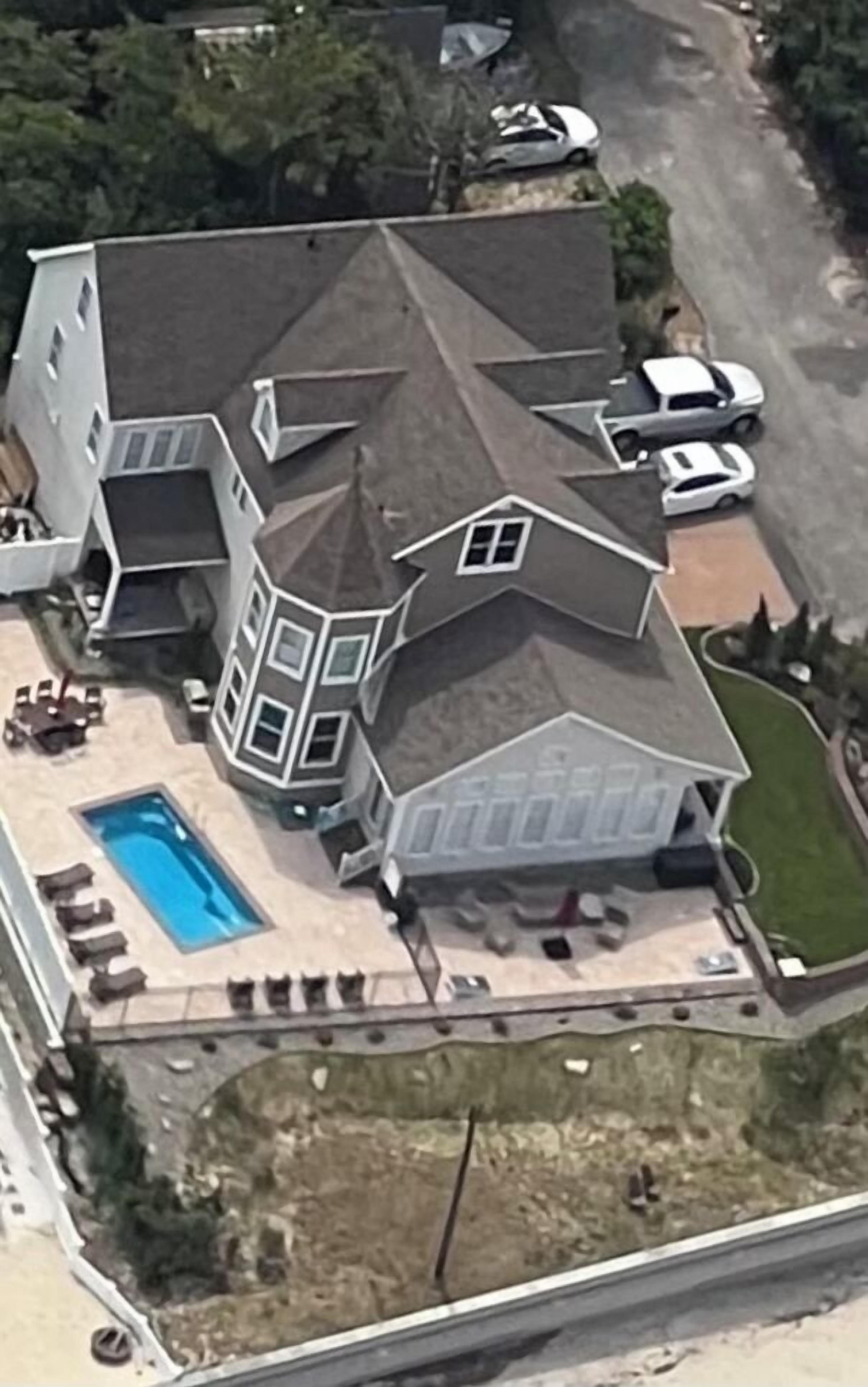 Ein großes, mehrgeschossiges Haus mit einem markanten Turm, einem Schwimmbad und einer Auffahrt mit geparkten Autos.