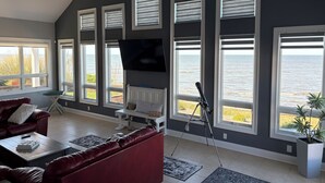 Een woonkamer met een groot raam met uitzicht op zee, een rode bank, een salontafel en een telescoop.
