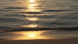Een zonsondergang boven een rustige zee met zachte golven die de kust bereiken.