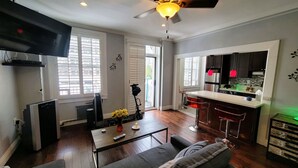 Ein modernes Wohnzimmer mit einer Couch, einem Couchtisch und einem Fernseher. Es gibt eine Küchenzeile mit einer Bar und einem Kühlschrank.