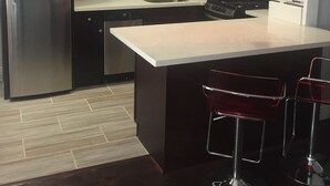 Eine moderne Küche mit dunklen Holzausführungen, Edelstahlgeräten, einer gefliesten Spritzschutzwand und roten Pendelleuchten.