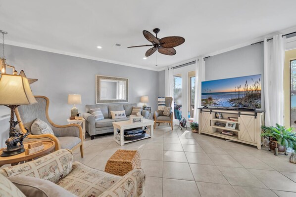 A spacious living room with a grey sofa, a coffee table, a TV, and a ceiling fan.