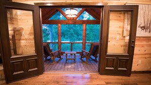 A wooden door leading to an outdoor deck with rocking chairs and a table. - Starry Respite: Hot Tub, 3 Fireplaces, Ping Pong, Foosball, Arcade, Pets allowed (Broken Bow)