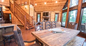 A wooden interior with a staircase, a dining table, and a fireplace. - Starry Respite: Hot Tub, 3 Fireplaces, Ping Pong, Foosball, Arcade, Pets allowed (Broken Bow)