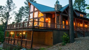 A log cabin with a wooden deck, large windows, and a stone chimney. - Starry Respite: Hot Tub, 3 Fireplaces, Ping Pong, Foosball, Arcade, Pets allowed (Broken Bow)