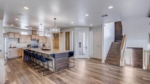 A modern kitchen with a central island, bar stools, and a staircase leading to another level. - The Beachside - Banyan Beach, Ocean View & Short walk to Beach (Port Aransas)