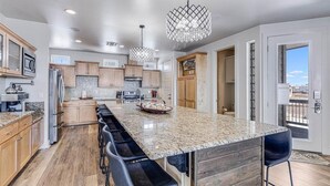 A spacious kitchen with granite countertops, wooden cabinets, and a large island with bar stools. - The Beachside - Banyan Beach, Ocean View & Short walk to Beach (Port Aransas)
