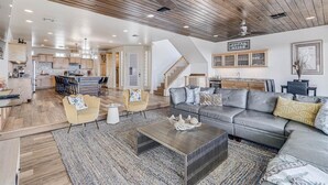 A spacious living area with a wooden ceiling, a grey sofa, a coffee table, and a dining area in the background. - The Beachside - Banyan Beach, Ocean View & Short walk to Beach (Port Aransas)